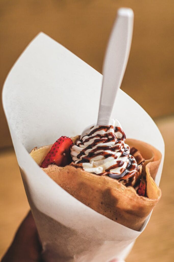 Close-up of a rolled crepe with strawberries, whipped cream, and chocolate drizzle.